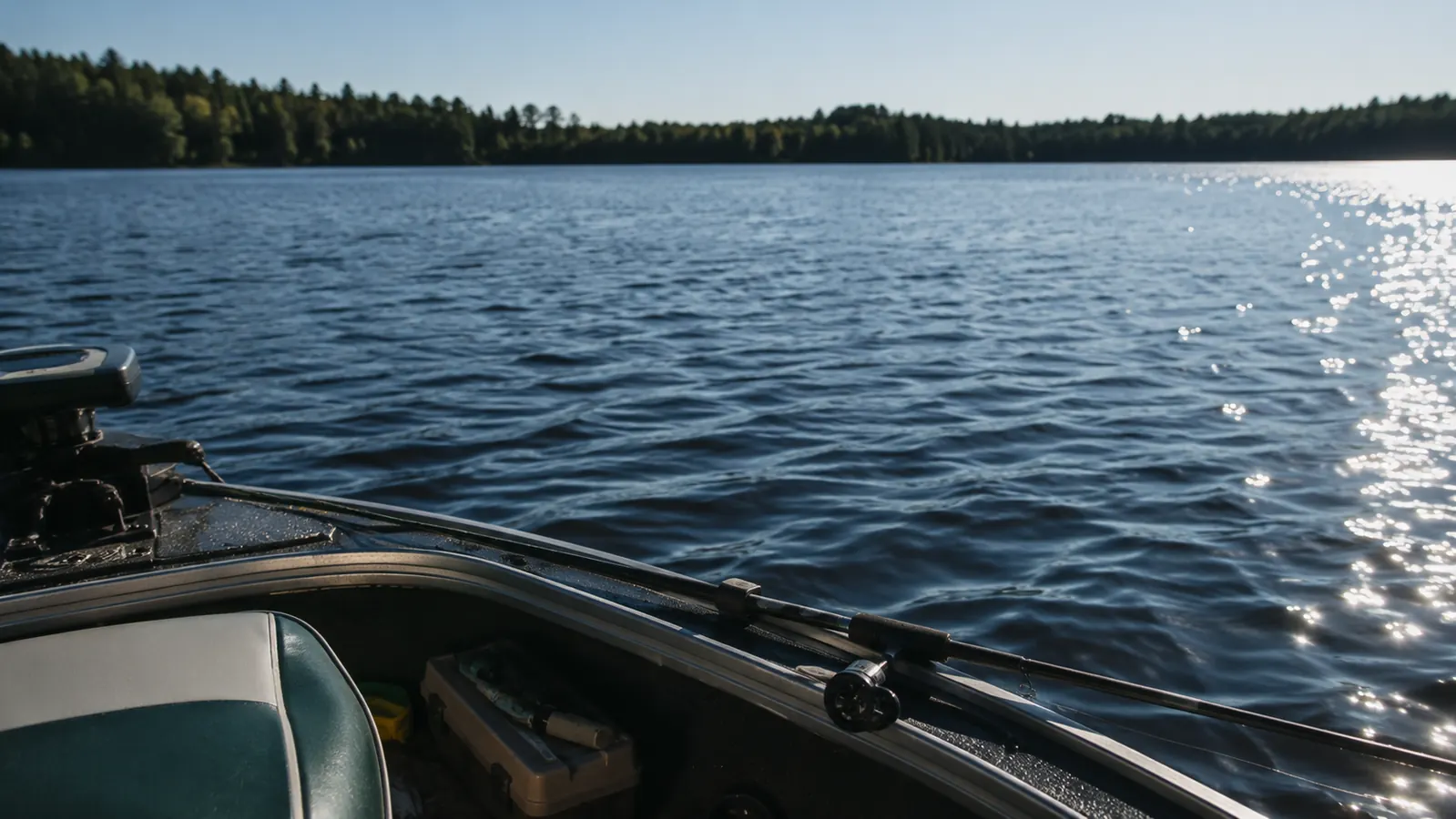 A calm lake seen from the bow seat at mid-morning, ripples on the water, a distant treeline, and a rod lying across the gunnel with the line going out